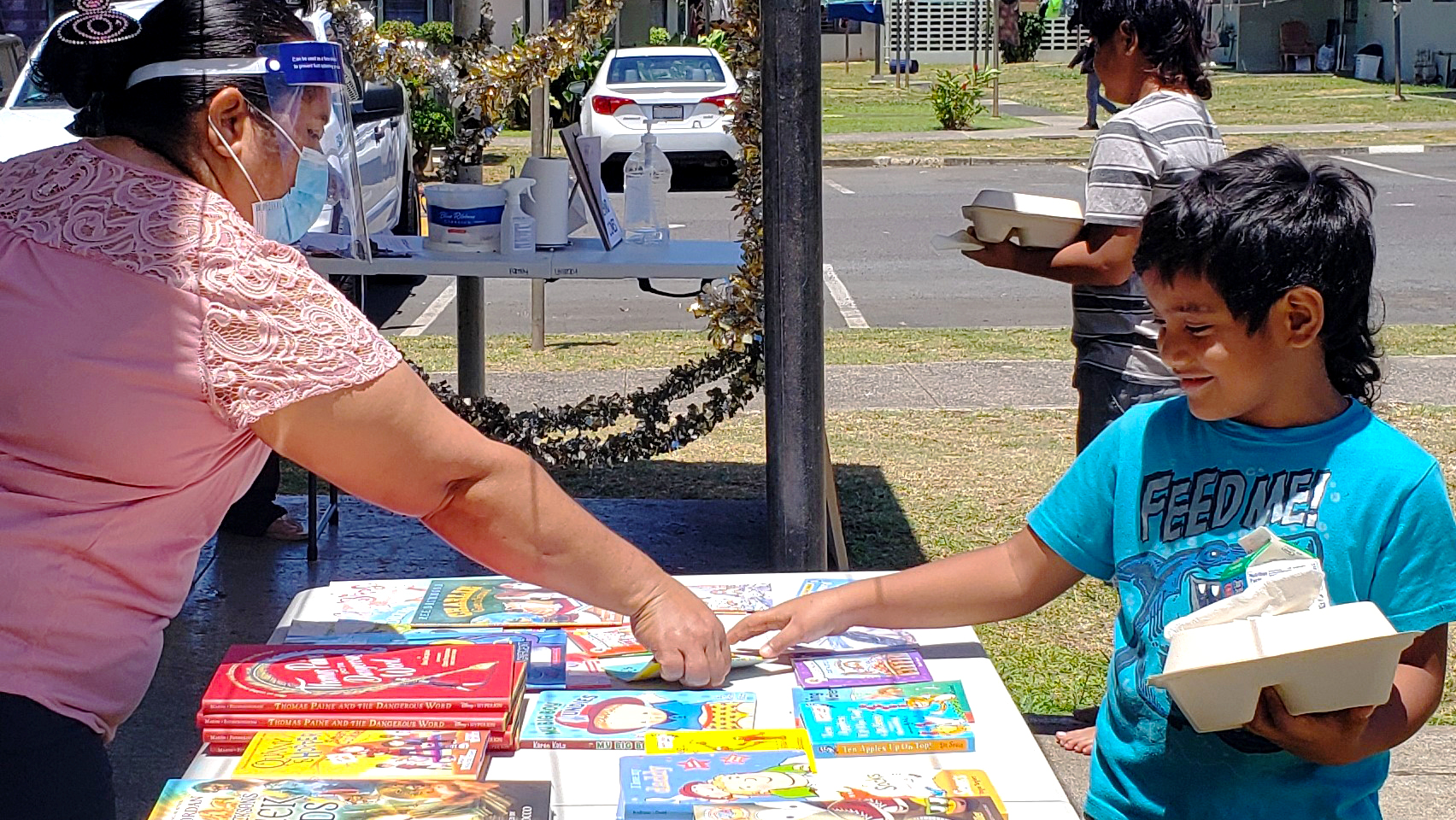 a Hawaii Literacy volunteer hands a book to a young boy during a book drive event