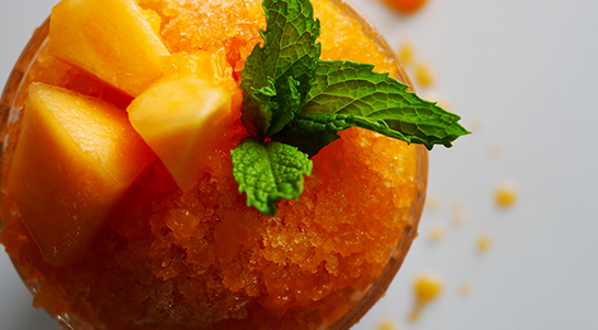 an overhead view of a deep-orange cantaloupe papaya granita served in an etched glass topped with green mint sprigs and light orange cantaloupe chunks
