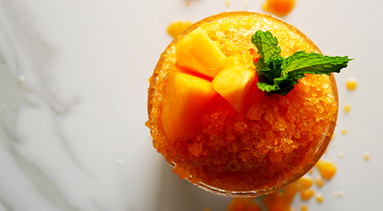 an overhead view of a deep-orange cantaloupe papaya granita served in an etched glass topped with green mint sprigs and light orange cantaloupe chunks