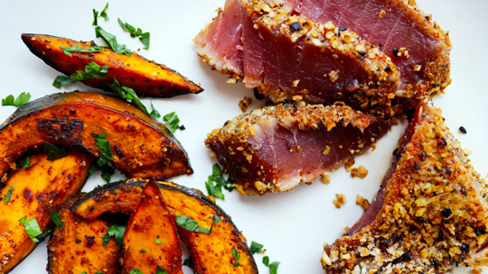 a close-up view of seared ahi crusted with panko and sesame seeds next to roasted kabocha squash wedges and a broiled lemon wedge